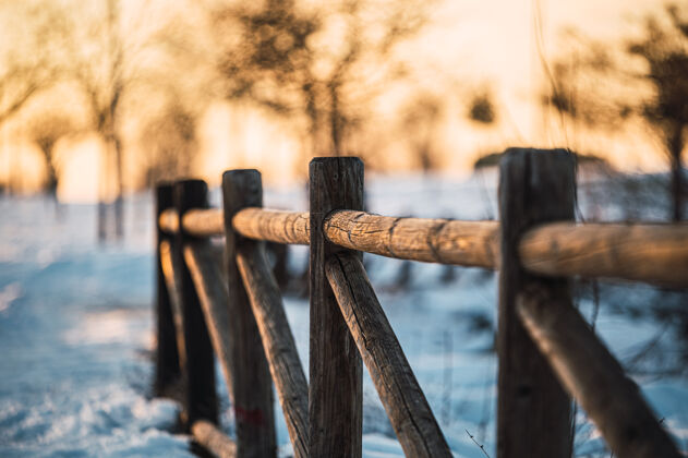 乡村冬天的景色 木栏杆靠近积雪覆盖的小路 穿过田野 夕阳下的乡村里没有叶子的树木安静自然草地