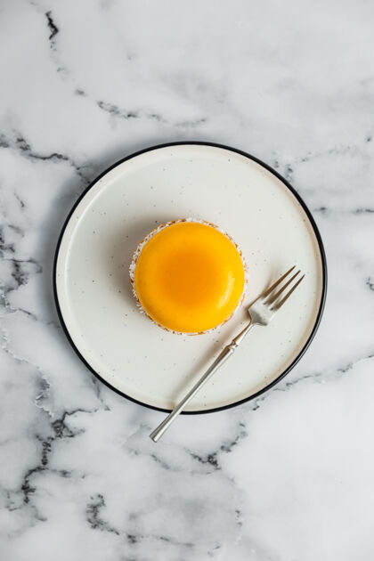 美食白色盘子上的黄色芒果慕斯蛋挞 甜点叉 顶视图面包房通风大理石