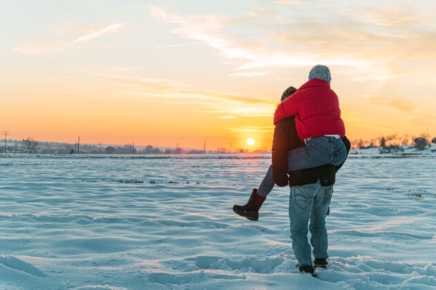 享受在雪乡 快乐的男人背着你的女朋友欢呼心爱的草地