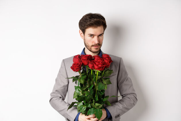 惊喜帅哥穿西装去约会 捧着一束红玫瑰对着镜头微笑 做情人节惊喜礼物 白色背景男朋友情感花