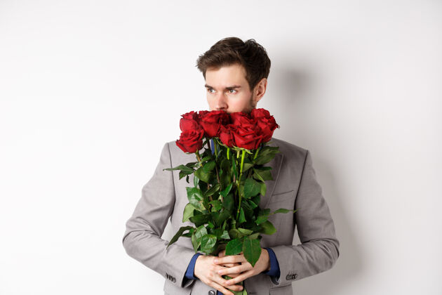 情感穿着西装的浪漫男人闻到一束玫瑰花的香味 站在白色的背景下 显得若有所思情人节的概念关系同性恋情人节