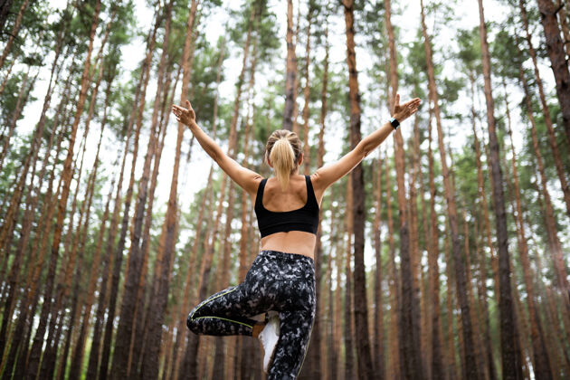 身体美丽的女人站在森林里做瑜伽锻炼和冥想的概念敬拜或举手夏天的松木主题后视图姿势体位森林