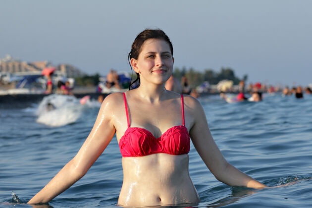 游泳一个年轻的白种女人 站在齐腰深的水里 海滩背景上有很多沐浴者和日光浴的人和游客人青少年年轻