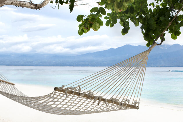 热带吊床悬挂在沙滩上的树木之间 背景是蔚蓝的巴厘岛海岸的吉利特拉万根岛风景天堂树