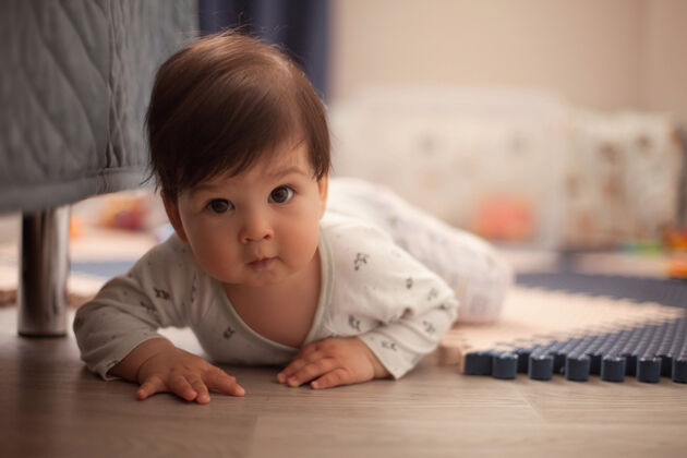 情绪穿着明亮的睡衣 一头黑发的漂亮男婴正在学习爬行 趴在托儿所的地板上婴儿床孩子黑发