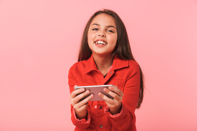 爱一个微笑的少女站在红色的墙上 一边用手机玩游戏室内玩黑发