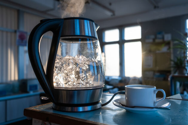 液体一壶透明的水在透过窗户的夕阳下沸腾透明壶茶壶