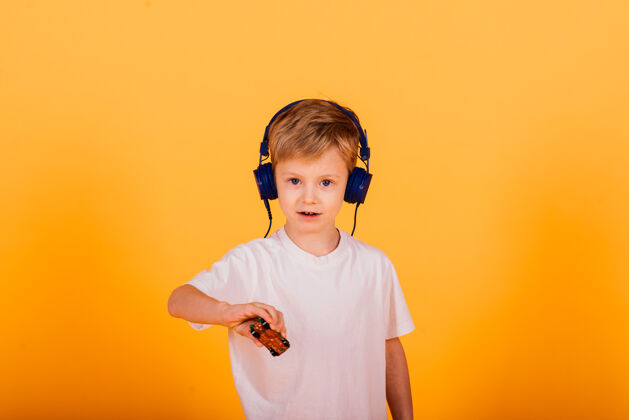 男孩小男孩戴着耳机听音乐 黄色的背景.儿童耳机里的童话故事欢呼男性音乐