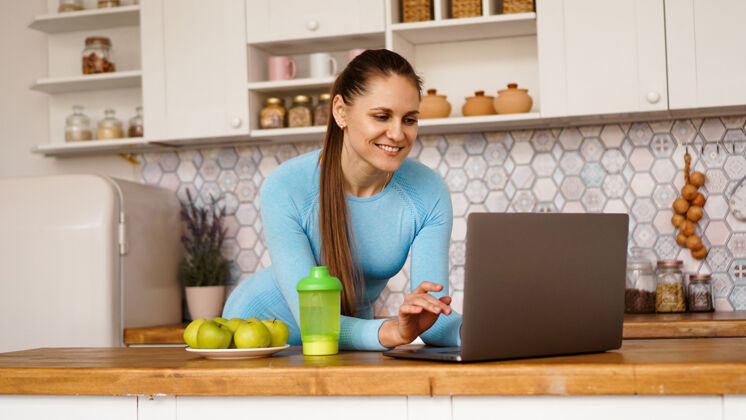 指向微笑的女人在现代厨房里使用电脑烹饪与健活理念一个女人正在寻找一个食谱或是在网上流微笑室内健康