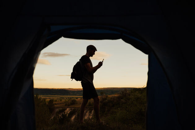 旅游年轻人在山上野营 站在帐篷旁边打短信放松冒险夏天