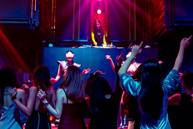 乐趣一群人随着舞台上dj的音乐节拍在迪斯科夜总会跳舞青年俱乐部女孩