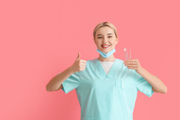 牙医带着工具的女牙医在彩色表面上竖起大拇指肖像牙釉质口腔