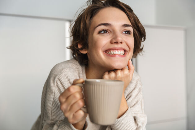 休闲微笑的年轻女子早上在厨房喝茶早餐站立白种人