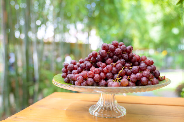 美味红葡萄放在踏步玻璃板上 独自站在户外花园里的木桌上模糊波基季节收获玻璃
