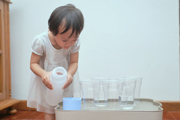 杯可爱的亚洲学步小女孩在家玩水桌玩得很开心 湿浇蒙台梭利学前实践生活活动 精细运动技能培养夏天家庭学校婴儿