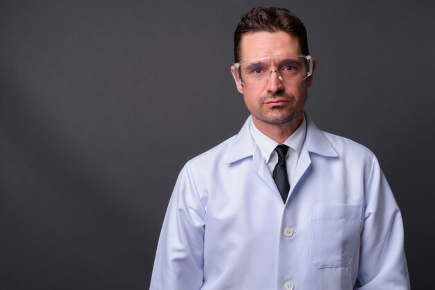 肖像英俊的大胡子男人 医生 科学家 戴着防护眼镜 挡在灰色的墙上眼镜保护安全