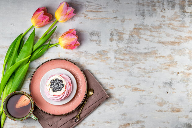 颜色一杯茶 草莓 巴甫洛娃蛋糕和白色木头上的粉红色郁金香慕斯杯子早餐