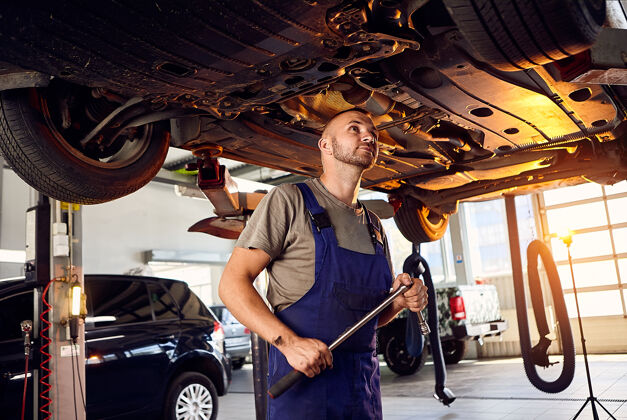 发动机帅气的汽车修理工在加油站检查汽车的传动装置悬架工业车间