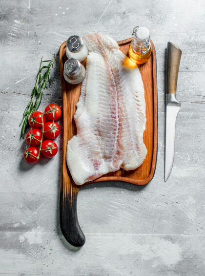 景观把鱼片放在砧板上 用刀 香料 油和西红柿放在盘子上分支机构白色质朴的桌子生的罗非鱼香料