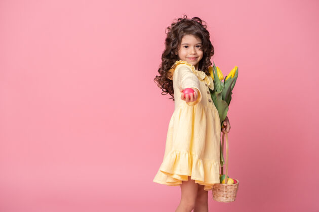 庆祝漂亮的小女孩拿着篮子 篮子里放着复活节彩蛋和郁金香 背景是粉红色的传统节日孩子