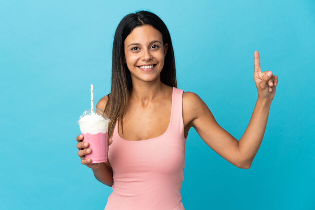 数字一位年轻的女士拿着草莓奶昔 伸出手指表示最好第一手势冰沙