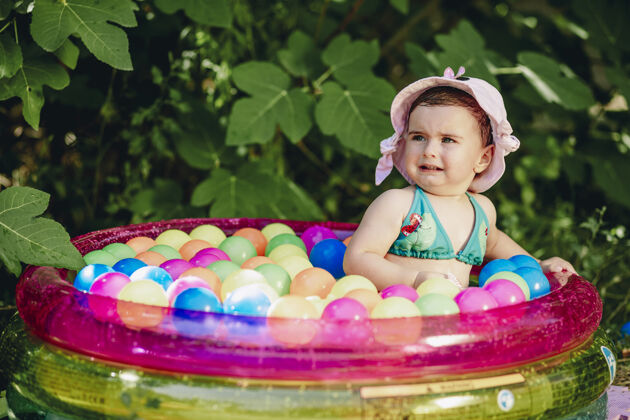 女婴可爱的宝宝戴着创意帽子 在满是五颜六色球的泳池里哭帽子颜色滴