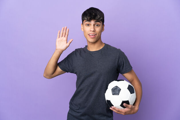 运动年轻的足球运动员在孤立的紫色墙壁上用手致意 表情愉快人比赛手势