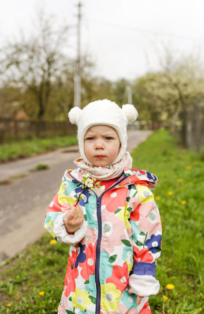 公园春天里 一个穿着鲜艳夹克的小女孩站在外面 手里拿着一枝春天开的白花美丽多彩夹克