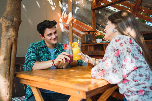 橘子一对幸福的情侣在酒吧里喝着两杯果汁举杯祝酒——年轻的情侣们看着对方的眼睛 微笑着享受他们的约会情人节情侣鸡尾酒