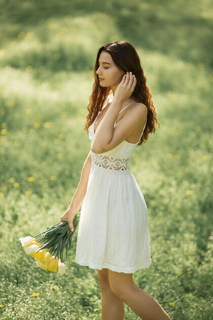女性一位身着白色礼服 手拿一束春花的迷人女子 在大自然的背景下漫步散步壁板花