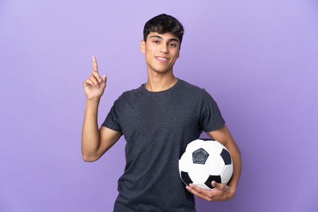 男性年轻的足球运动员男子在孤立的紫色背景下展示和举起手指表示最好的比赛训练运动员