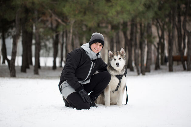 夹克冬季森林里的快乐男人狗.to和狗玩西伯利亚哈士奇山笑声松树