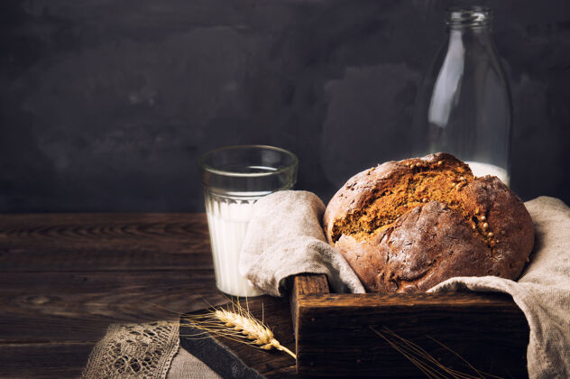 乡村在旧木桌上放着一瓶牛奶和芫荽籽自制的乡村黑面包农业木板混凝土