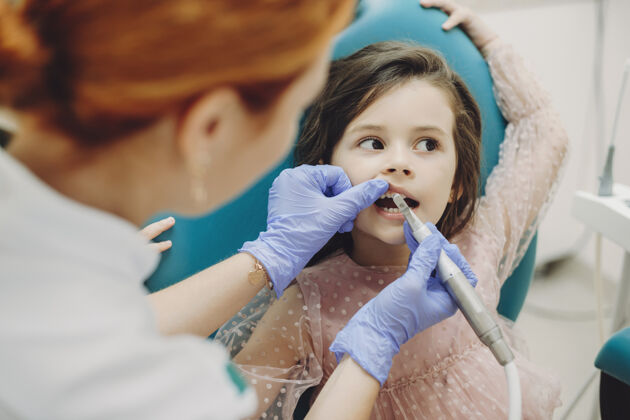 椅子可爱的小女孩做牙齿手术的肖像 而她是用手臂从口腔科的座位 并看着别处办公室牙医医生