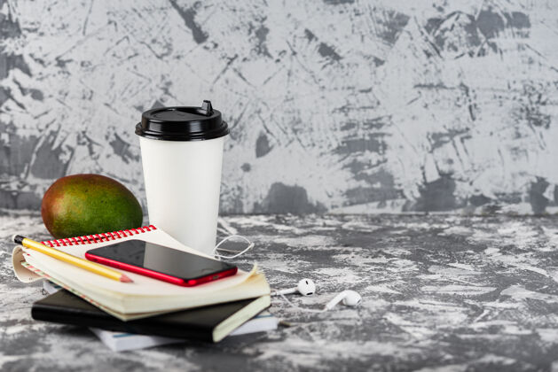 纸杯工作或教育去吧咖啡杯子 芒果 红色的智能手机和一堆放在灰色石头上的记事本表.copy空间对象自由职业者桌子