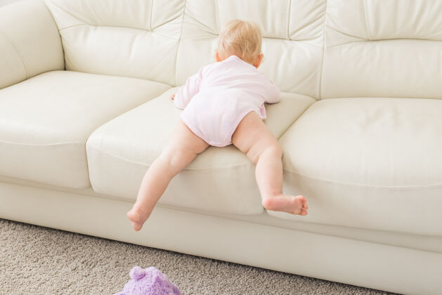 客厅童年 婴儿期和人的概念-快乐的小女婴在家里沙发边玩婴儿期攀岩幼儿