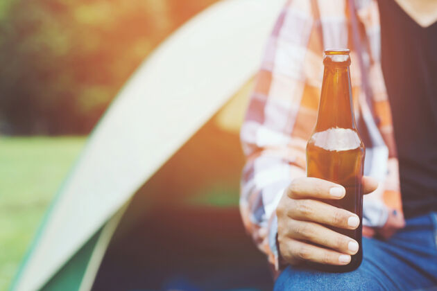 徒步旅行旅行三个年轻的朋友在一起玩 在远足营地放松 喝啤酒 喝彩和酒瓶享受假期野营旅游探险概念聚会乐趣液体