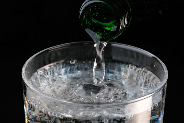 飞溅纯碳酸水从一个瓶子倒进一个透明的玻璃在一个黑色的墙壁特写宏饮用玻璃苏打水刷新