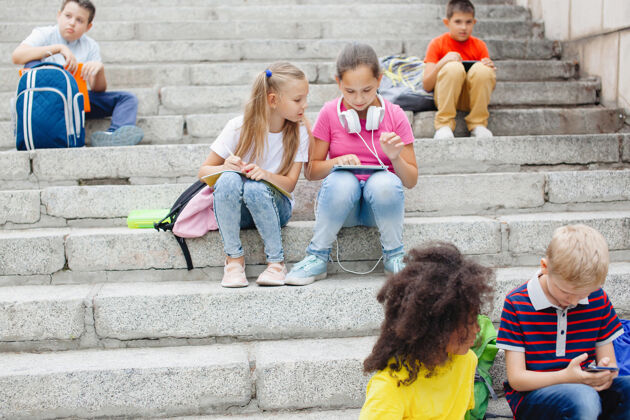 学校一群不同民族的小学生 穿着五颜六色的衣服坐在石头上台阶青少年说话 用耳机听音乐 看书女性教育可爱