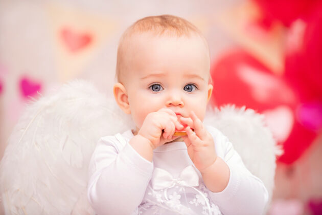 羽毛一个长着白色羽毛翅膀吃心形饼干的女婴的画像红色嫩无辜