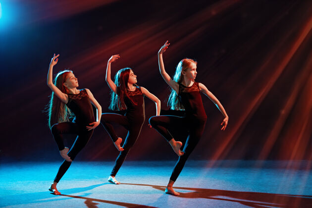 青少年三个穿着紧身服装的芭蕾舞女孩在黑色背景下跳舞训练实践活动