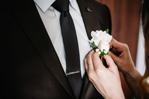 粉彩新娘的手把新郎放在婚礼的夹克上花束婚礼概念日期丝带花束