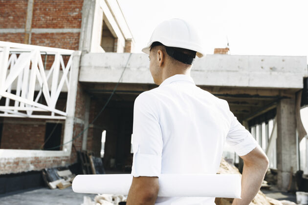 手一位年轻的拿着大楼的平面图 正在检查大楼的工作情况衬衫工人专业