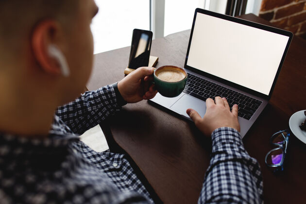 办公桌拿着一杯咖啡和耳机在笔记本电脑前工作的男人家模糊背景高高质量的照片商务男性年轻