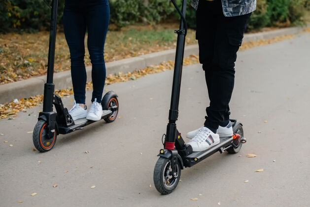 腿一个男孩和一个女孩的腿骑电动踏板车特写电动滑板车城市移动