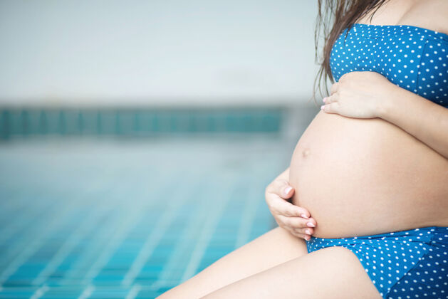 户外穿着泳衣内衣的孕妇坐在床边池使用用手触摸肚子宝贝年轻怀孕的女人站在床上户外运动增强体质容易生父母婴儿女性