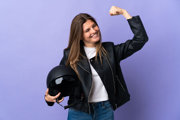 人年轻的斯洛伐克女子手持摩托车头盔在紫色背景上庆祝胜利司机摩托车手头盔