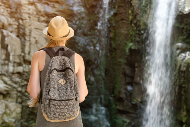旅行女孩背着背包 戴着帽子 看着瀑布.view从后面站立背部景观