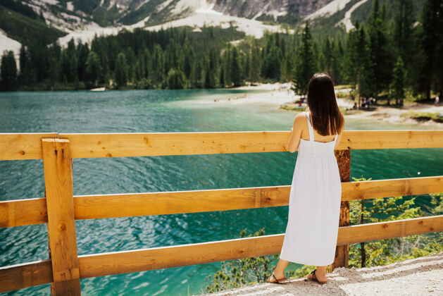 五颜六色一个穿着白色裙子的女孩站在湖边的翡翠湖水的背面女人黑发年轻