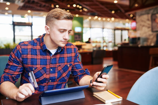 坐着严肃的年轻人通过智能手机上的应用程序在线购物 并用信用卡支付学生阅读微笑